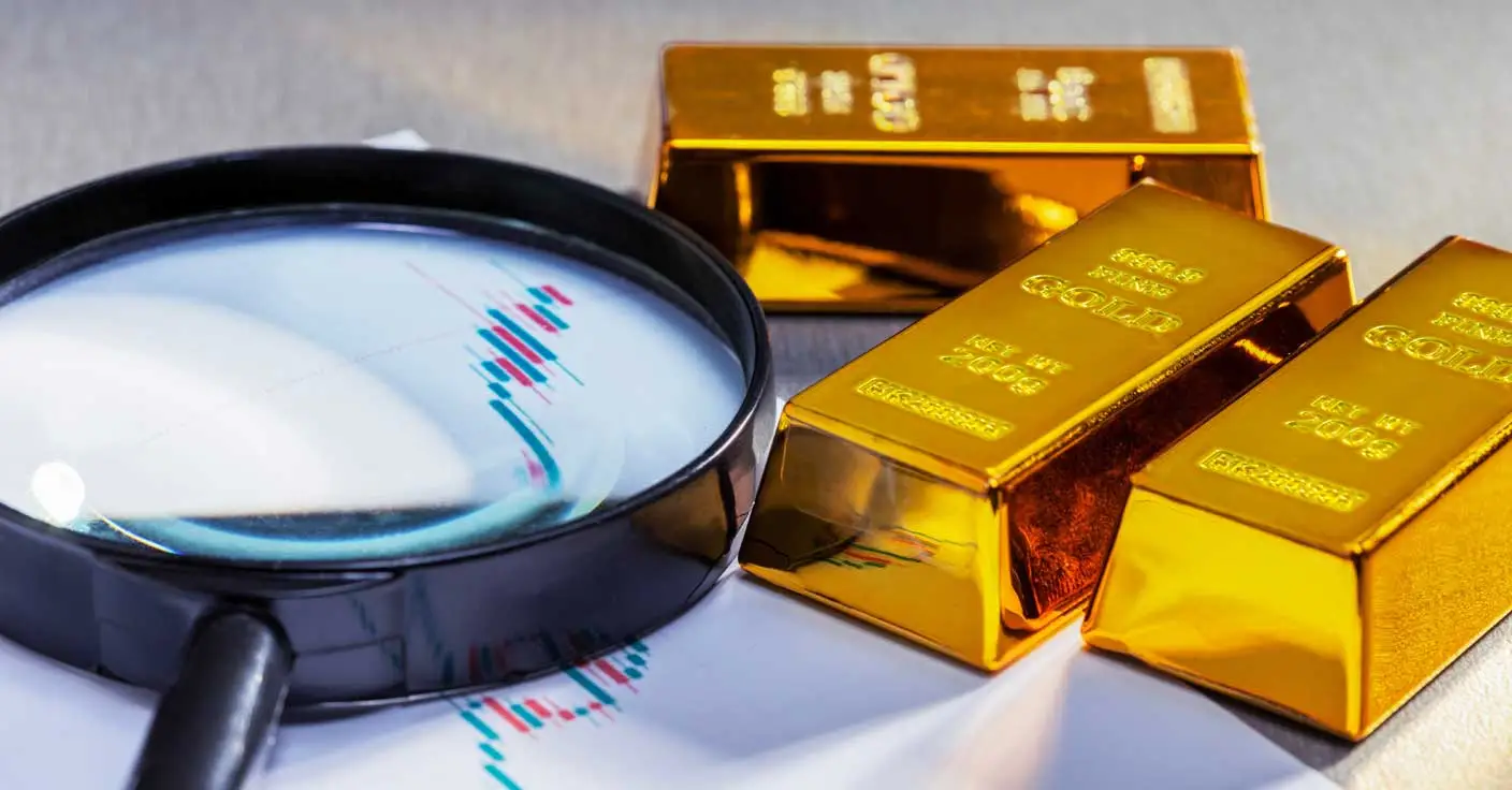 Goldbarren und Lupe auf einer gedruckten Kursgrafik des Goldpreises